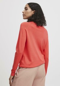 Maglione a maglia corallo con scollo a girocollo e maniche lunghe, dotato di polsini a coste e vestibilità comoda, abbinato a pantaloni beige chiaro.