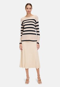 Gestreepte trui in crèmekleur en marineblauw, gebreide stof, bootnek, lange mouwen. Gecombineerd met een beige, middellange rok en nude sandalen.