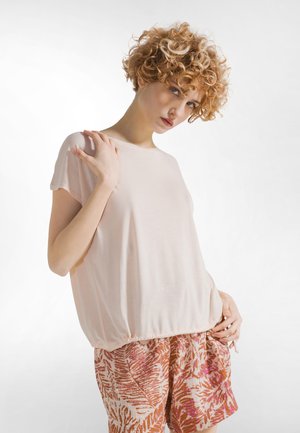 Lichtroze top met korte mouwen, losse pasvorm en geplooide zoom, gecombineerd met korte broek met aardse tinten en tropische bladmotieven.