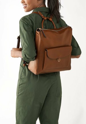 Sac à dos en cuir marron avec une poignée supérieure, une poche frontale et des bretelles réglables. Texture lisse et forme rectangulaire.