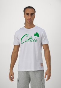 Biała bawełniana koszulka z zielonym napisem "Celtics" oraz grafiką koniczyny. Projekt zawiera przyszytą metkę na dole.
