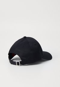 Black cotton baseball cap with a curved brim, adjustable strap at the back, and a smooth texture. Notable design includes a rounded top.