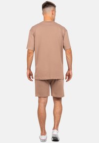 Set di t-shirt a maniche corte beige e pantaloni corti abbinati, realizzati in morbido cotone. Vestibilità comoda con un design semplice e una leggera trama.