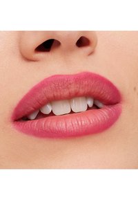 Gros plan sur des lèvres avec un rouge à lèvres rose mat. La texture est lisse avec des contours bien définis, mettant en valeur des dents blanches naturelles et un teint de peau doux.