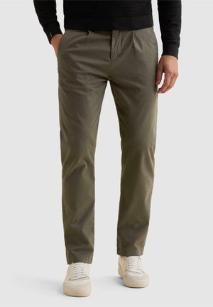 Homme portant un pantalon droit vert olive et des baskets blanches, les mains dans les poches, montré de la taille aux pieds.