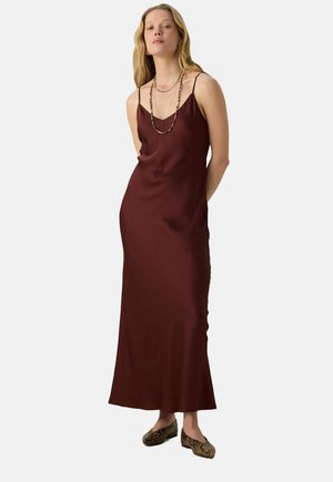 Bordeaux satijnen slipdress met dunne spaghettibandjes, een rechte halslijn en een vloeiende silhouet, met een subtiele glans. G gedragen met een gepatternde schoenen.