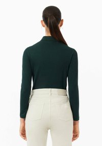 Mörkgrön långärmad skjorta med krage, parat med ljusa högmidjade jeans. Slät textur, åtsittande design och minimal detaljering.