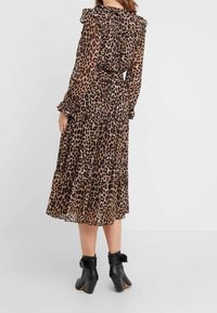 Femme portant une robe en imprimé léopard à manches longues et longueur midi avec des volants, assortie de bottes noires à la cheville avec des boucles.