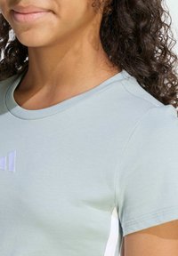 Svetlomodré bavlnené tričko s okrúhlym výstrihom, krátkymi rukávmi a bielymi bočnými akcentmi, s malým vyšitým logom na prednej strane.