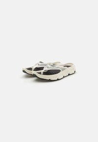 Mesh slip-on sko med et hvitt og svart fargeskjema, med en teksturert såle og avrundet design. Lett og pustende materiale.