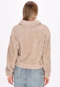 Pullover beige, plush, a costine con collo e maniche lunghe. Il tessuto ha una texture morbida e una vestibilità rilassata. Vista posteriore mostrata.