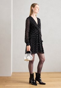 Abito nero con maniche lunghe, dettagli argentati e vita annodata. Abbinato a stivaletti neri lucidi e una piccola borsa argentata.
