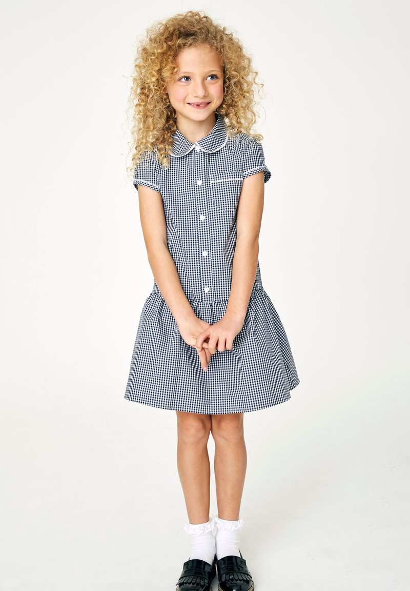 Haljina na mornarsko plave i bijele karo uzorke s kratkim rukavima, ovratnikom, prednjim gumbima i naboranim suknjom. Uparena s bijelim čarapa s volančićima i crnim cipelama.