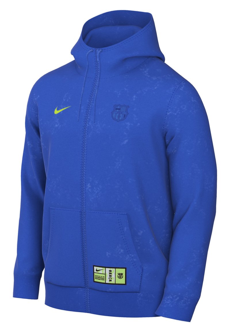 Sudadera azul con cremallera hecha de un tejido suave, con un alto cuello, bolsillos frontales, logo de Nike en amarillo neón y emblema del club de Barcelona.