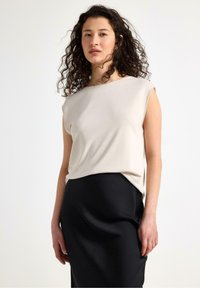 Kortærmet, lyse beige top i blødt stof med en afslappet pasform, parret med en sort, tætsiddende nederdel, der fremhæver glatte teksturer og et enkelt design.