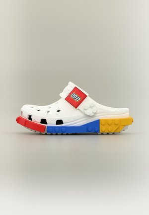 Hvid slip-on klodsko med ventilationshuller, LEGO-logo på remmen og en sål designet med røde, blå og gule LEGO-klodsmønstre.