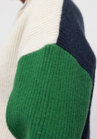 Knitted sweater featuring a color block design with cream, green, and navy sections. The textured fabric has a ribbed appearance.