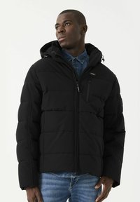 Chaqueta de plumas negra con capucha, diseño acolchado, cierre de cremallera, bolsillo en el pecho y puños elásticos. Llevada sobre una camisa de mezclilla, tejido texturizado.