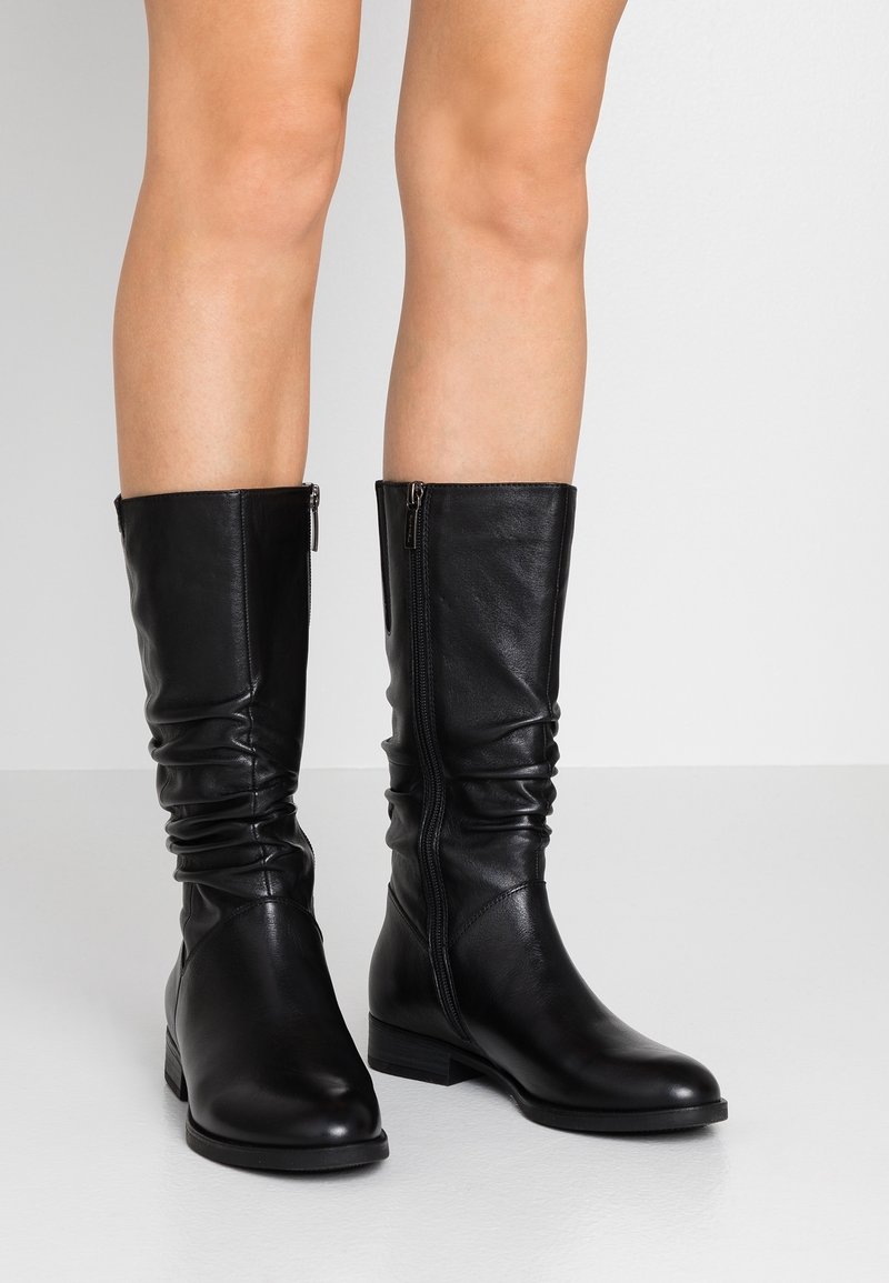 Svarta läderknä-stövlar med en avslappnad design, sidodragkedja, platt klack och slät textur. Enkel silhuett och funktionella detaljer.