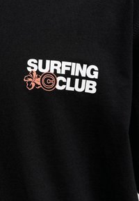 Μαύρο ύφασμα με λευκό κείμενο "SURFING CLUB" και ένα ροζ λουλούδι ιβίσκου με σύμβολο πνευματικών δικαιωμάτων αντί για το "O" στο "CLUB".