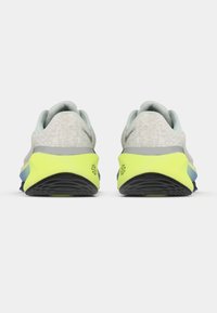 Svijetlosive atletske cipele s teksturiranom gornjom površinom, fluorescentno žutom potplatom i plavim naglascima, s zaobljenim dizajnom i jastučićem na peti.