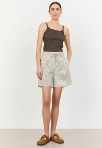 Brown ribbed tank top paired with high-waisted cream shorts featuring vertical stripes, belt, and pleats. Brown suede slip-on shoes.