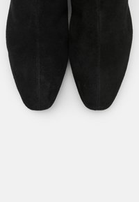 Botas de tobillo de ante negro con diseño de punta afilada, textura suave y detalles de costura mínimos, vistas desde arriba.