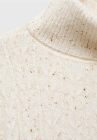 Pull à col roulé en maille couleur crème avec motif torsadé et taches brunes réparties sur le tissu.