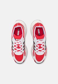Piros és fehér sportcipők, hálós felsőrésszel, fekete részletekkel és fehér fűzőkkel. Párnázott talppal rendelkezik, és "adizero" logóval van ellátva.