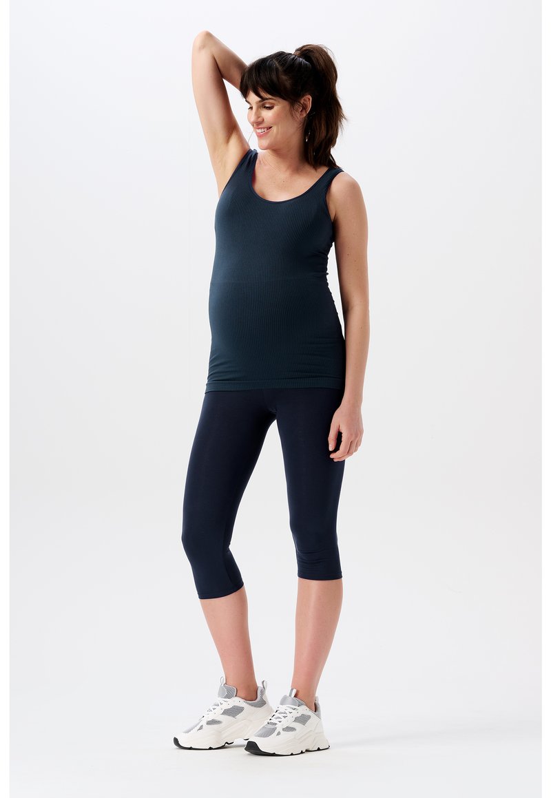 Zwangerschaps sportoutfit: donkergroen geribbeld tanktop, marineblauwe capri leggings, witte sneakers. Strak ontwerp met rekbare stof voor comfort.