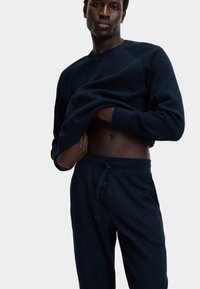 Set di felpa e pantaloni blu navy in tessuto testurizzato. La felpa presenta un collo a girocollo; i pantaloni hanno un elastico in vita e un cordoncino.