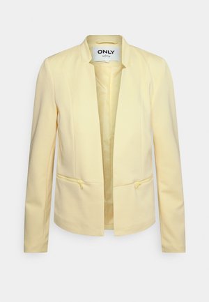 Blazer giallo in materiale a coste, con design senza colletto, apertura frontale e due tasche con zip sul davanti. Fodera interna liscia.