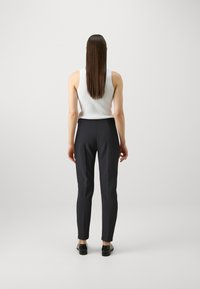 Un débardeur blanc à côtes associé à un pantalon noir ajusté. Le pantalon présente une texture lisse et est fuselé aux chevilles.