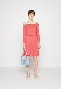 Vestido coral ombro a ombro com mangas longas, cintura ajustada e saia ampla; combinado com uma bolsa azul clara e sandálias de plataforma bege.