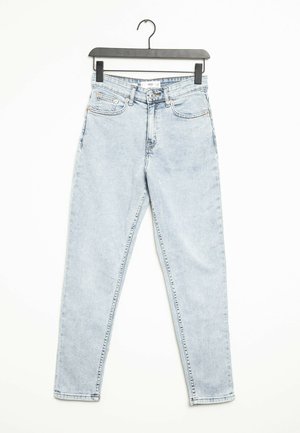 Jasnoniebieskie, wysokowalne, dopasowane jeansy wiszące na czarnym plastikowym wieszaku na białym tle.