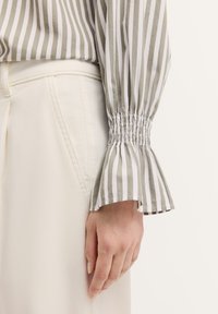 Gestreifte Bluse in grün und weiß mit gerafften Glockenärmeln, kombiniert mit weißen, hoch sitzenden Hosen. Baumwollmaterial mit glatter Textur.