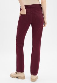 Bordeauxfarbene gerade geschnittene Hose mit glatter Textur, fünf Taschen und mittelhohem Bund. Kombiniert mit beigen Schuhen.