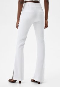 Vita utsvängda byxor med en mjuk textur, två bakfickor och sprund på fållen, med en figursydd hög midja.
