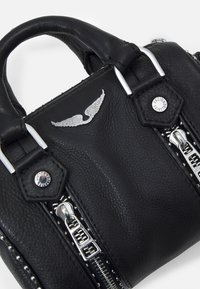 Mustan nahkalaukun, jossa on hopeinen varustus, vetoketjuyksityiskohtia ja koristeellinen siipisymbooli. Teksturoitu pinta ja vahvistetut saumat.