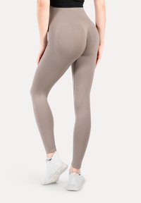 Beżowe legginsy z wysokim stanem, gładką strukturą i przylegającym krojem, w połączeniu z białymi butami sportowymi. Widoczne przeszycia.