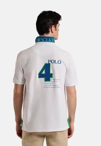 Camisa polo blanca con un cuello azul y verde, gran número "4" verde y el texto "POLO" en la parte de atrás. Incluye detalles en texto azul.