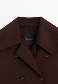 Burgundowa wełniana kurtka z wyciętym kołnierzem, podwójnym zapięciem na guziki i czarnymi guzikami. Wewnątrz znajduje się metka z napisem "Massimo Dutti".