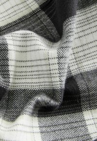 Plaid fabric in black, white, and gray tones with a soft texture and varying check patterns, featuring thin and thick lines throughout.