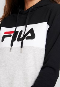 Sudadera con capucha en blanco y negro con parte inferior gris, que presenta un destacado logo de FILA, cordones ajustables y una textura suave.
