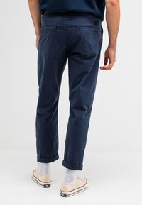 Marineblauwe, lichte chinos met een ontspannen pasvorm, opgerolde manchetten en achterzakken. Gepaard met beige sneakers en witte sokken.