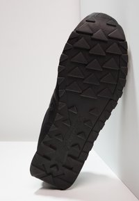 Black athletic shoe sole featuring a textured rubber surface with triangular patterns for traction, along with a brand logo.