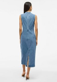 Denim kleita ar pieguļošu siluetu, bez piedurknēm, vidēja garuma, ar aizmugurējo šķēlumu un augstu dekoltē. Materiāls ir gaiši zils džins.