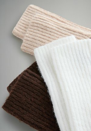 Tři kusy žebrované pletené látky v jemných texturách: světle béžová, bílá a tmavě hnědá, s výraznými žebry a útulným vzhledem.