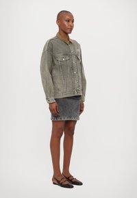 Gray denim jacket with a brown corduroy collar, front pockets, paired with a fitted gray denim skirt and patterned flat shoes.