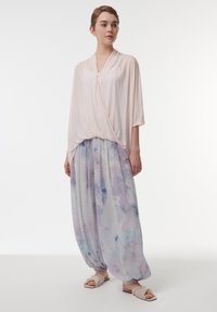 Lichtroze gedrapeerde top met een v-hals, in combinatie met lichtblauwe en paarse geplooide broek met een aquarelpatroon, gedragen met zachte slippers.